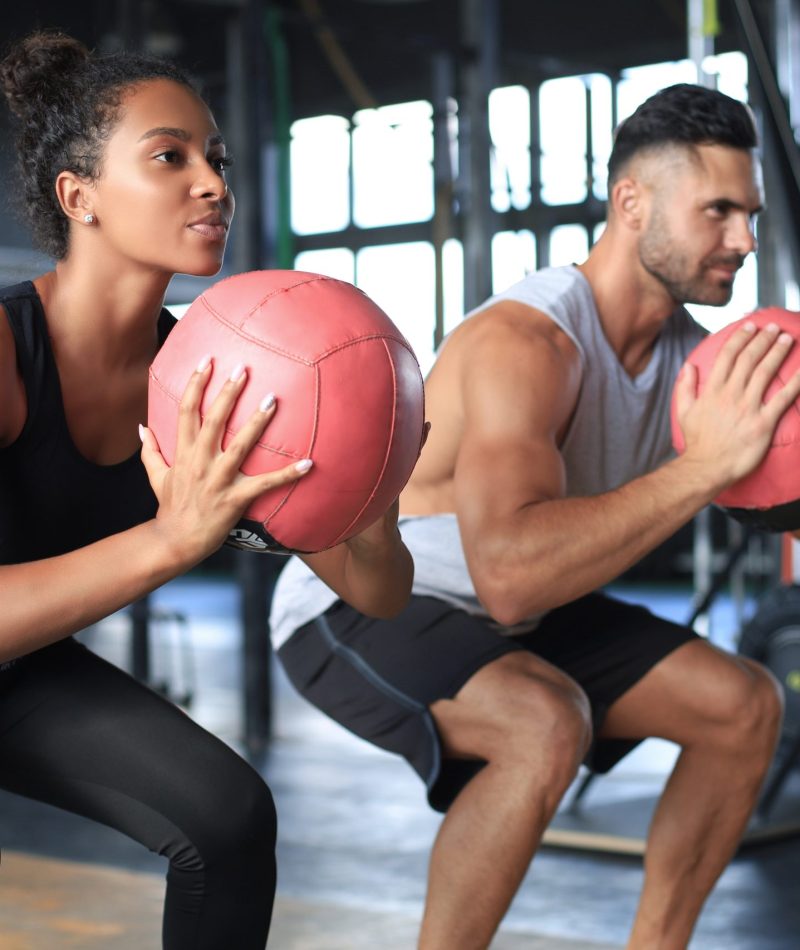 Beautiful young sports couple is working out with medicine ball in gym