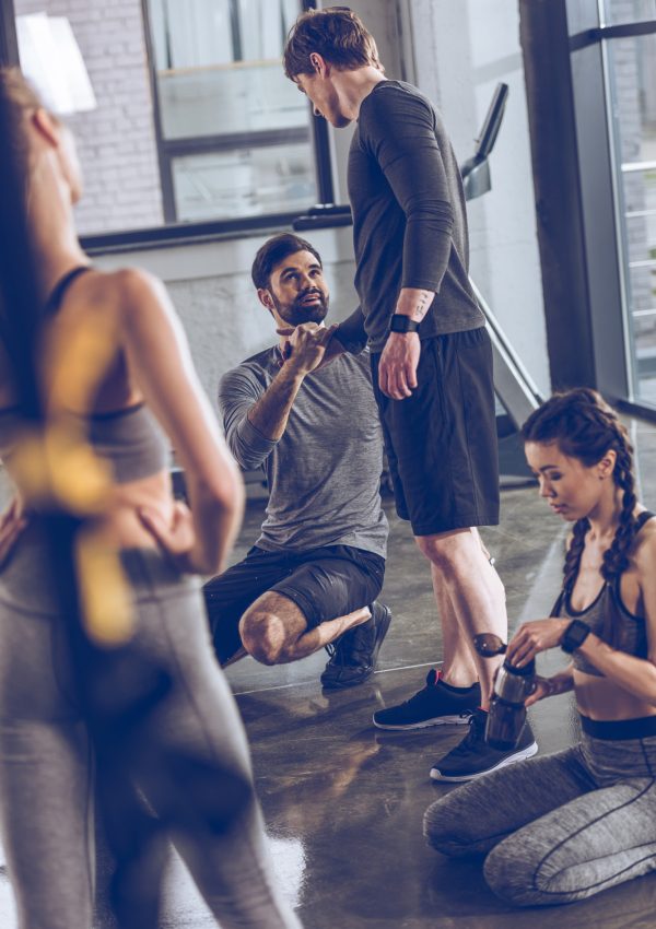 group of athletic young people in sportswear sitting on floor and resting at the gym, group fitness